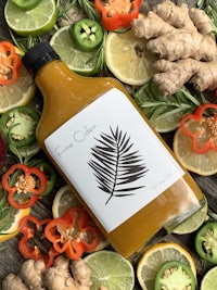 a bottle of juice surrounded by lemons, limes, and ginger